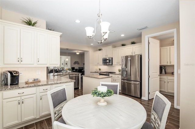 kitchen with light stone countertops, hanging light fixtures, dark hardwood / wood-style flooring, kitchen peninsula, and appliances with stainless steel finishes