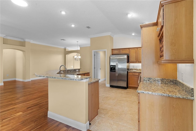 kitchen with stainless steel fridge, crown molding, lofted ceiling, decorative light fixtures, and a kitchen island with sink