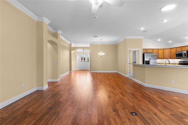 unfurnished living room with ceiling fan with notable chandelier, lofted ceiling, dark wood-type flooring, and crown molding