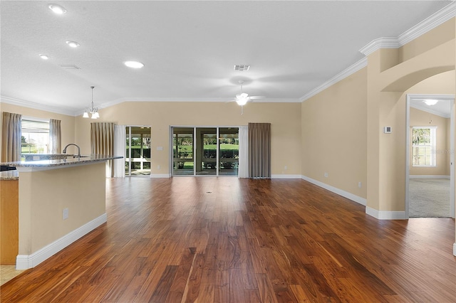 unfurnished living room featuring ceiling fan with notable chandelier, lofted ceiling, ornamental molding, and dark wood-type flooring