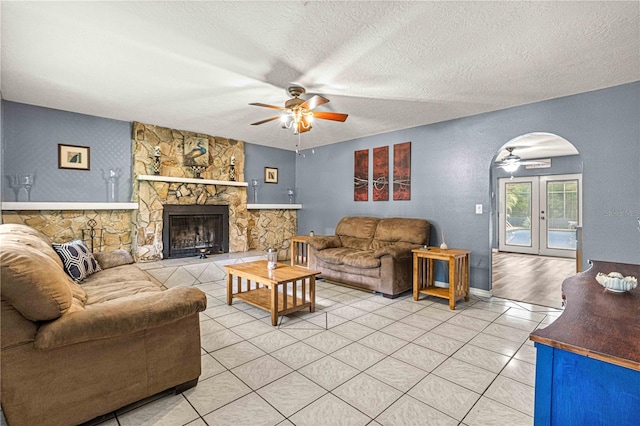 living room with ceiling fan, a fireplace, tile patterned flooring, and a textured ceiling