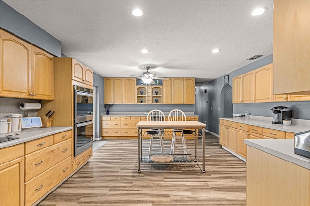 kitchen with light brown cabinetry, double oven, ceiling fan, light hardwood / wood-style floors, and a textured ceiling