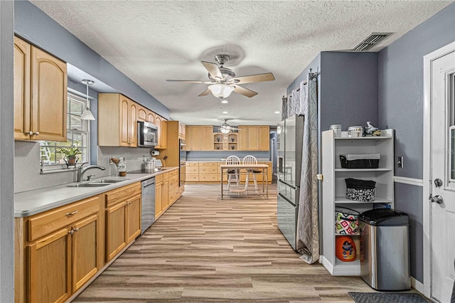 kitchen with sink, hanging light fixtures, light wood-type flooring, ceiling fan, and stainless steel appliances