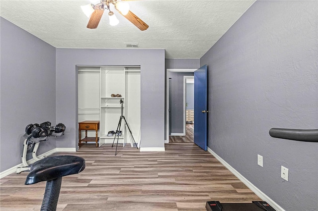 workout area featuring hardwood / wood-style flooring, ceiling fan, and a textured ceiling