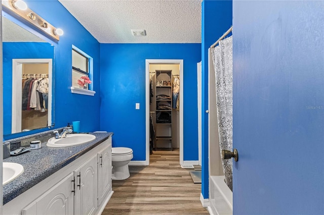 full bathroom featuring wood-type flooring, vanity, toilet, a textured ceiling, and shower / bath combo with shower curtain