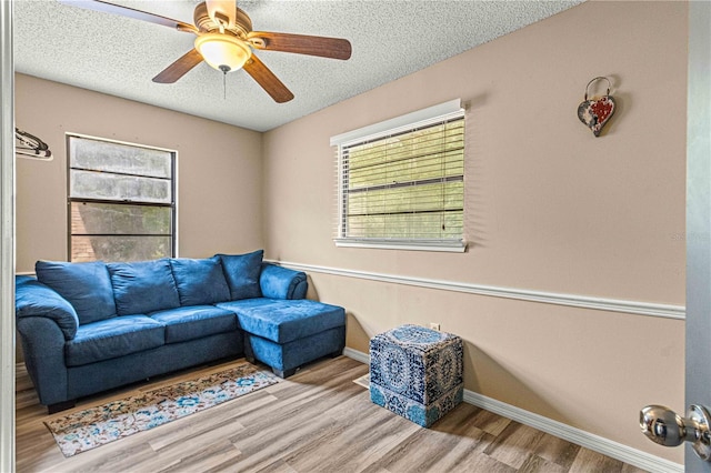 living room with ceiling fan, a textured ceiling, and light hardwood / wood-style floors