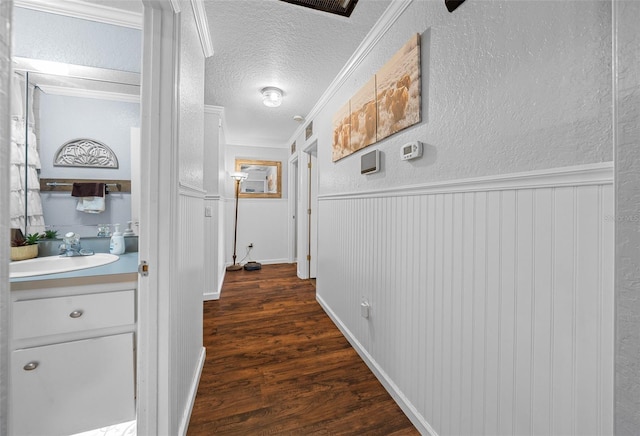 hallway with crown molding, dark hardwood / wood-style flooring, a textured ceiling, and sink