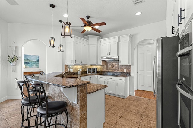 kitchen with light tile patterned floors, a breakfast bar area, white cabinetry, stainless steel appliances, and decorative backsplash