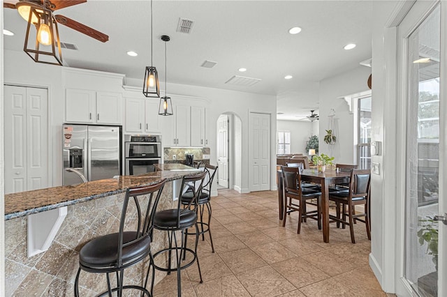 kitchen featuring a breakfast bar, white cabinetry, dark stone countertops, ceiling fan, and stainless steel appliances