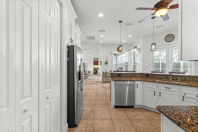 kitchen featuring appliances with stainless steel finishes, white cabinetry, sink, dark stone counters, and hanging light fixtures