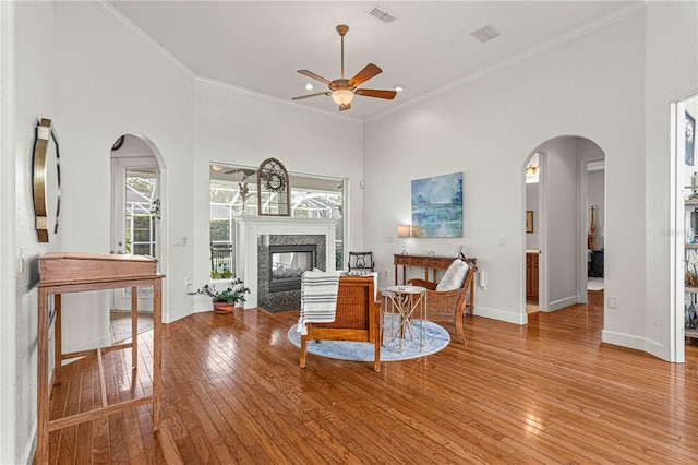 living room with crown molding, a high ceiling, ceiling fan, light hardwood / wood-style floors, and a premium fireplace