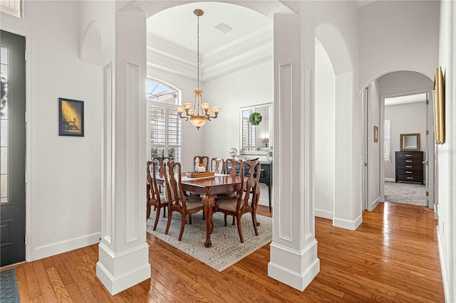 dining area with an inviting chandelier, wood-type flooring, a raised ceiling, and ornate columns