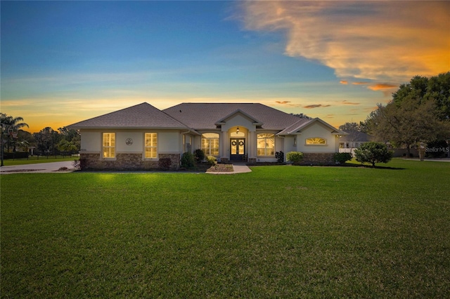 view of front of property featuring stone siding, a lawn, and stucco siding