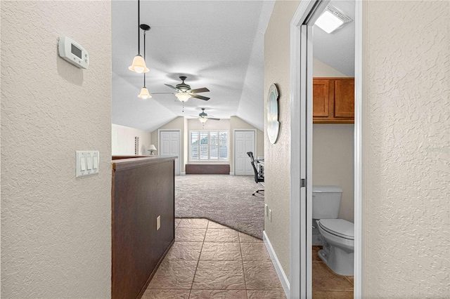 corridor with baseboards, carpet, vaulted ceiling, a textured wall, and a textured ceiling