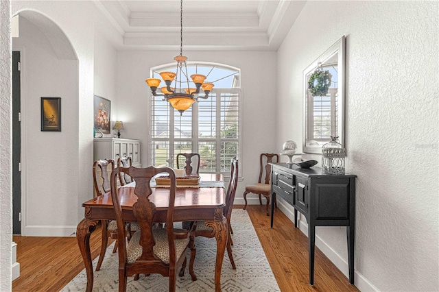 dining room featuring crown molding, arched walkways, light wood-type flooring, and a raised ceiling