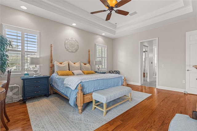 bedroom with a raised ceiling, wood finished floors, and ornamental molding