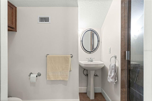 bathroom with a shower with shower door, visible vents, a sink, a textured ceiling, and baseboards