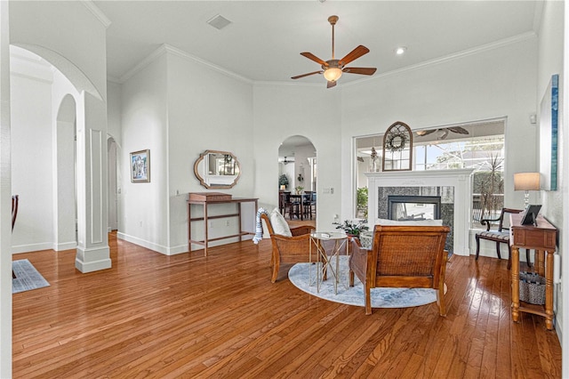 living room featuring a ceiling fan, hardwood / wood-style floors, arched walkways, a fireplace, and baseboards