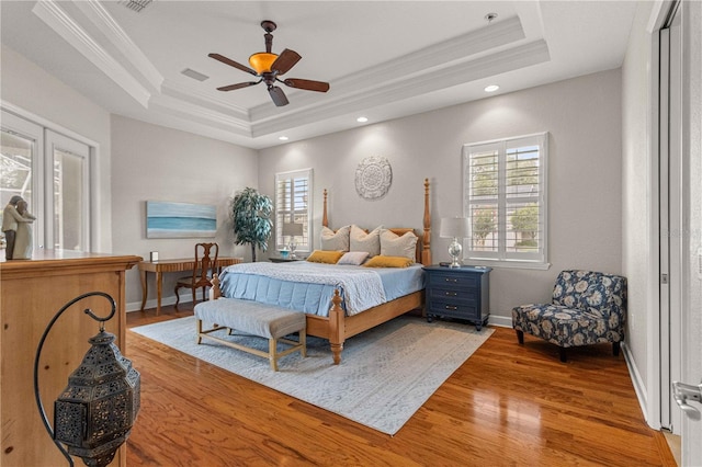 bedroom featuring a raised ceiling, light wood-style flooring, and ornamental molding