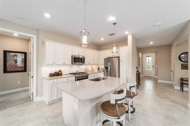 kitchen featuring decorative light fixtures, sink, an island with sink, stainless steel appliances, and white cabinets