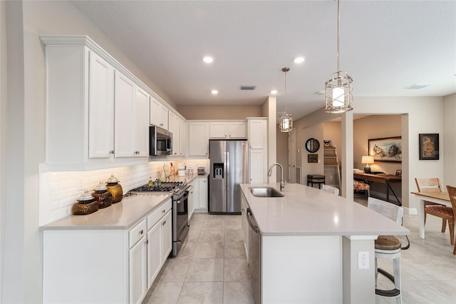 kitchen with an island with sink, appliances with stainless steel finishes, sink, and pendant lighting