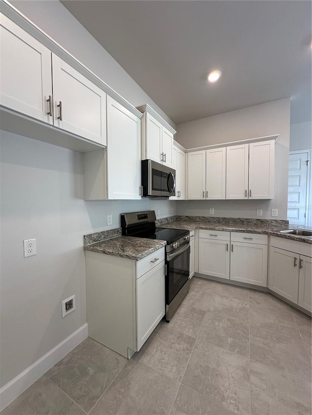 kitchen featuring white cabinets, stainless steel appliances, dark stone counters, and sink