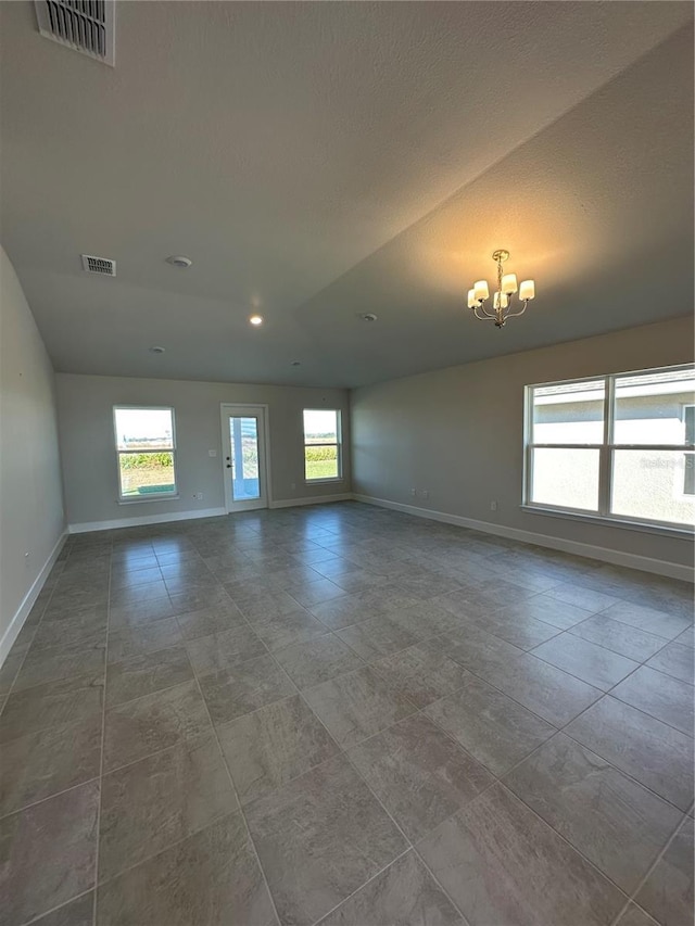 empty room with a healthy amount of sunlight, vaulted ceiling, and a chandelier