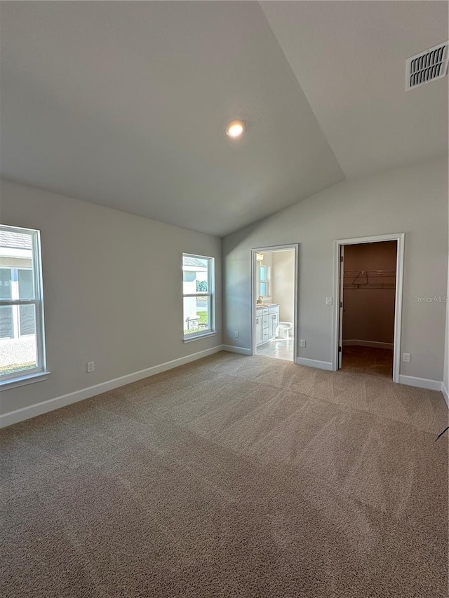 unfurnished bedroom with ensuite bath, a spacious closet, light colored carpet, lofted ceiling, and a closet