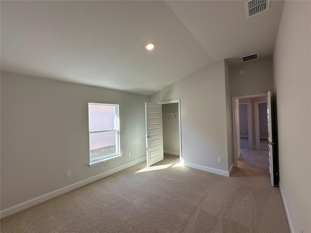 unfurnished bedroom featuring a spacious closet, light colored carpet, lofted ceiling, and a closet