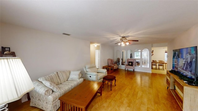 living area with arched walkways, light wood-style flooring, visible vents, and a ceiling fan