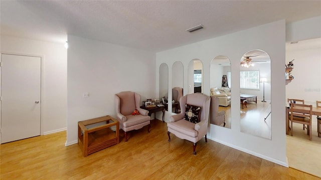 sitting room featuring ceiling fan, arched walkways, light wood-style floors, and visible vents