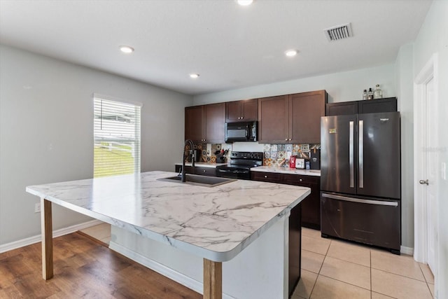 kitchen featuring a center island with sink, backsplash, black appliances, dark brown cabinetry, and sink