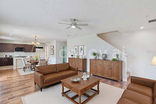 living room with ceiling fan with notable chandelier, a textured ceiling, and light wood-type flooring