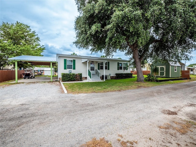 ranch-style house featuring a front yard, a porch, a carport, and a storage shed