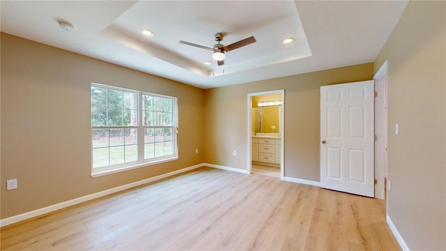 unfurnished bedroom with ceiling fan, ensuite bathroom, a raised ceiling, and light hardwood / wood-style floors