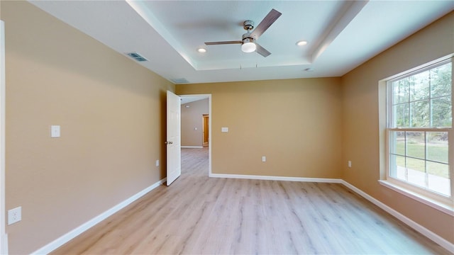 unfurnished room featuring ceiling fan, light hardwood / wood-style floors, and a tray ceiling