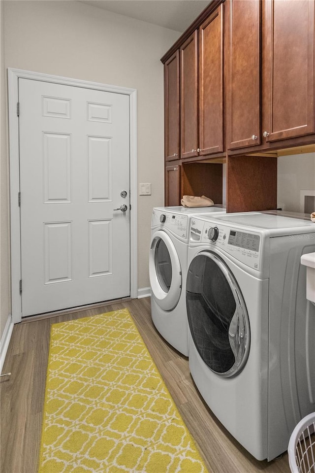 clothes washing area with washer and clothes dryer, light wood-type flooring, and cabinets