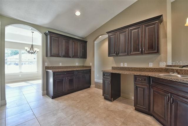 kitchen with vaulted ceiling, dark brown cabinetry, sink, and an inviting chandelier