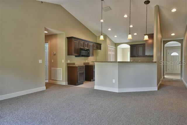 kitchen featuring dark brown cabinetry, high vaulted ceiling, light colored carpet, and decorative light fixtures