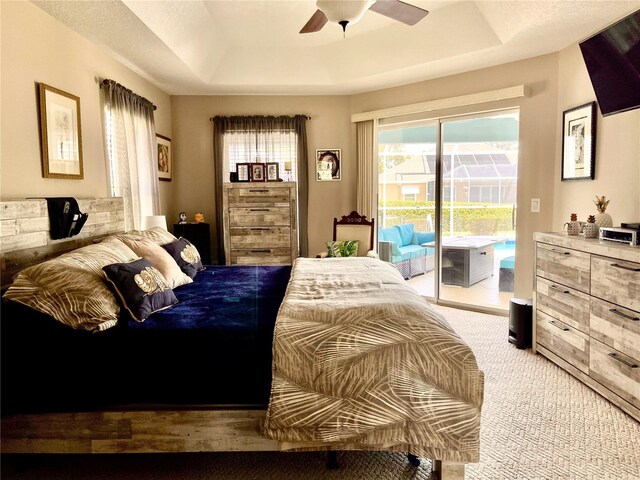 carpeted bedroom with a tray ceiling, access to exterior, and ceiling fan