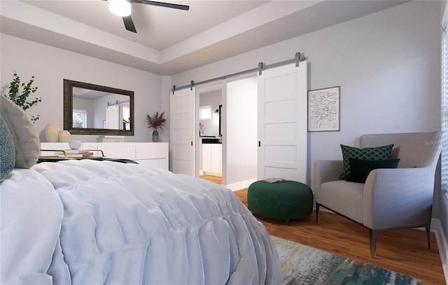 bedroom with ceiling fan, a barn door, a raised ceiling, ensuite bathroom, and hardwood / wood-style flooring