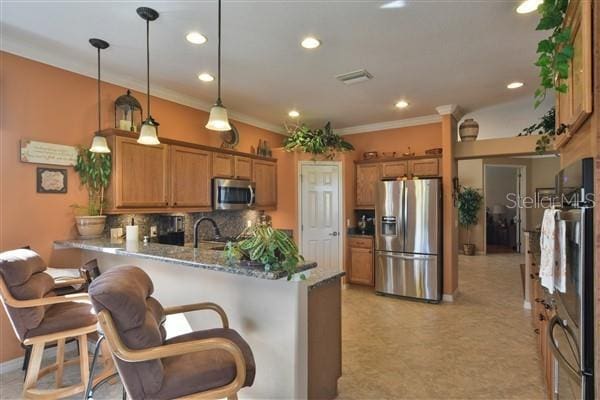 kitchen featuring hanging light fixtures, stainless steel appliances, kitchen peninsula, a kitchen bar, and decorative backsplash