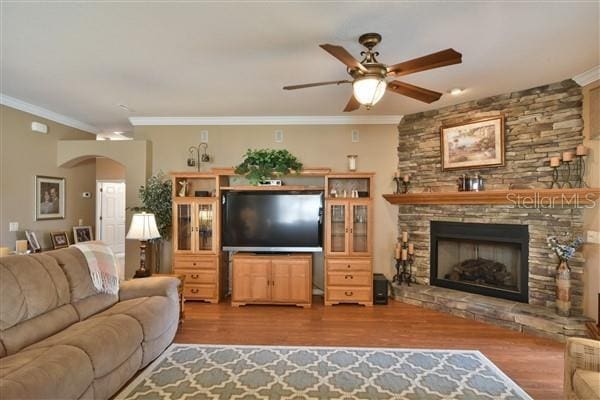 living room with a stone fireplace, crown molding, ceiling fan, and hardwood / wood-style flooring