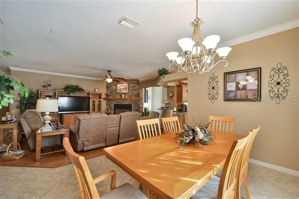 dining area featuring ceiling fan with notable chandelier, a large fireplace, and crown molding