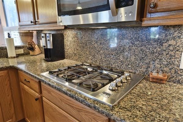 kitchen with backsplash, dark stone counters, and stainless steel gas stovetop