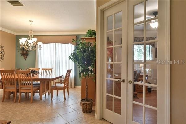 dining room with an inviting chandelier, light tile patterned floors, ornamental molding, and french doors