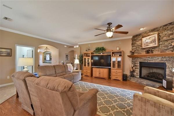 living room with a fireplace, light wood-type flooring, ceiling fan, and crown molding