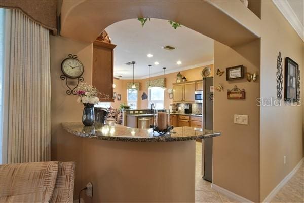 kitchen featuring kitchen peninsula, ornamental molding, decorative light fixtures, dark stone countertops, and light tile patterned flooring