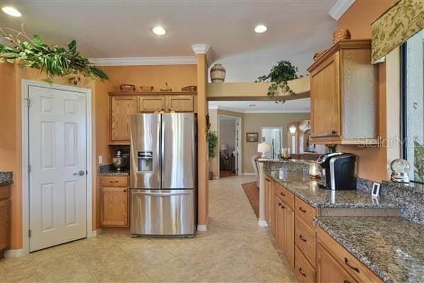 kitchen featuring stainless steel refrigerator with ice dispenser, ornamental molding, and dark stone counters