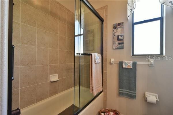 bathroom with plenty of natural light and bath / shower combo with glass door